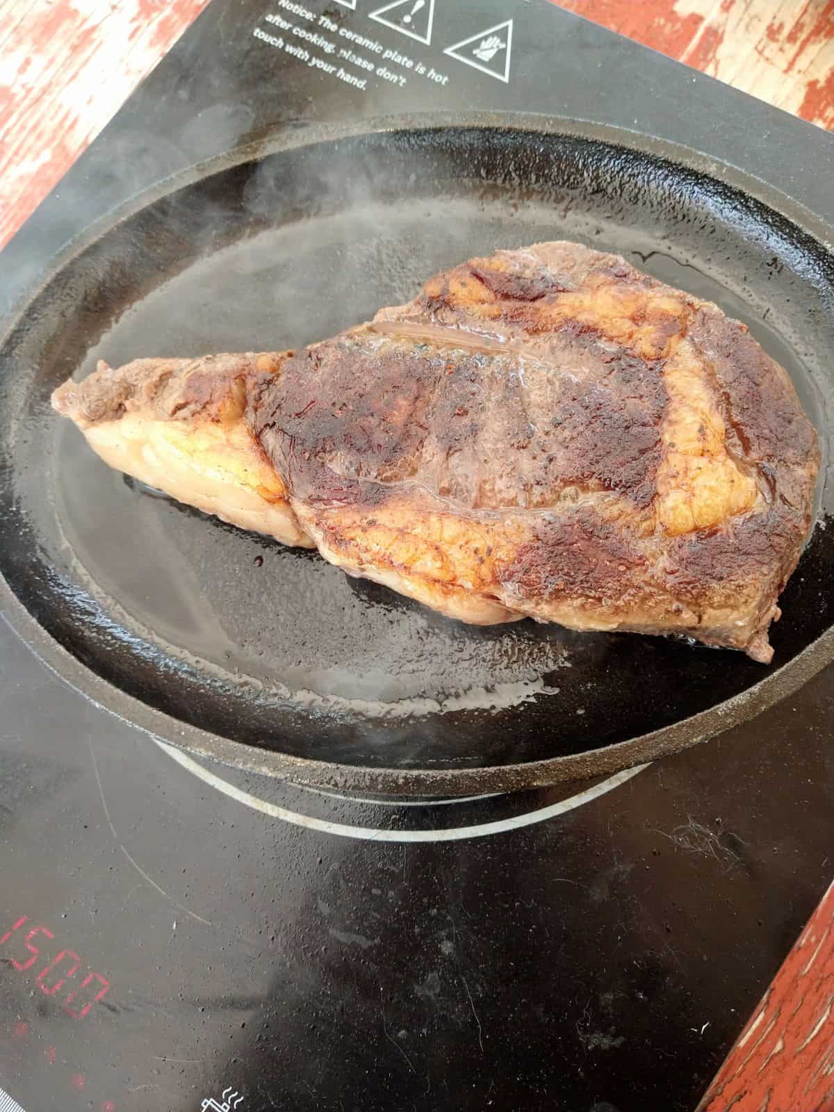 Searing a Bison Ribeye steak in a cast iron skillet using an induction cooktop.