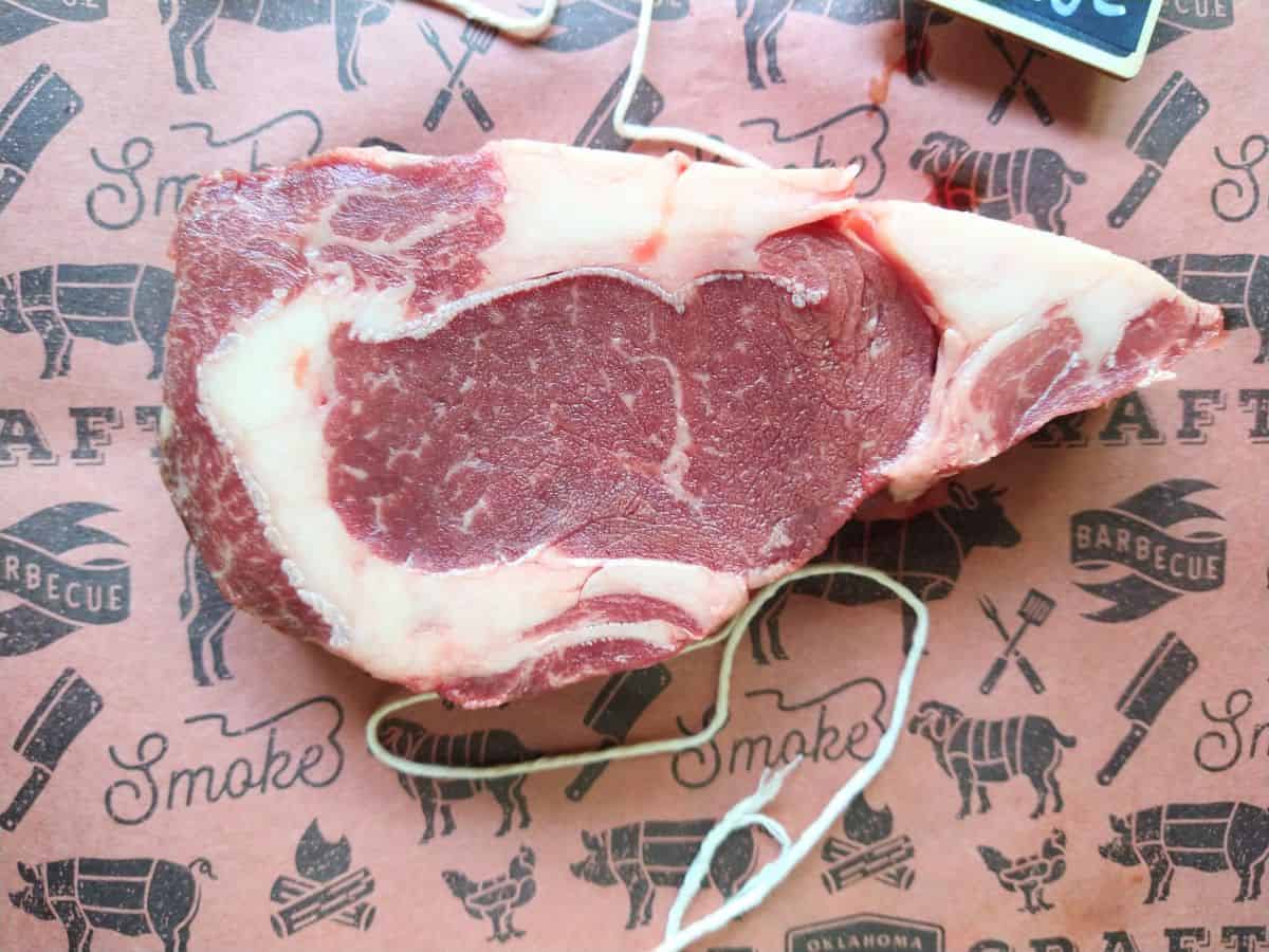 A close up of a raw bison ribeye steak on a piece of butcher paper with string underneath the steak. 