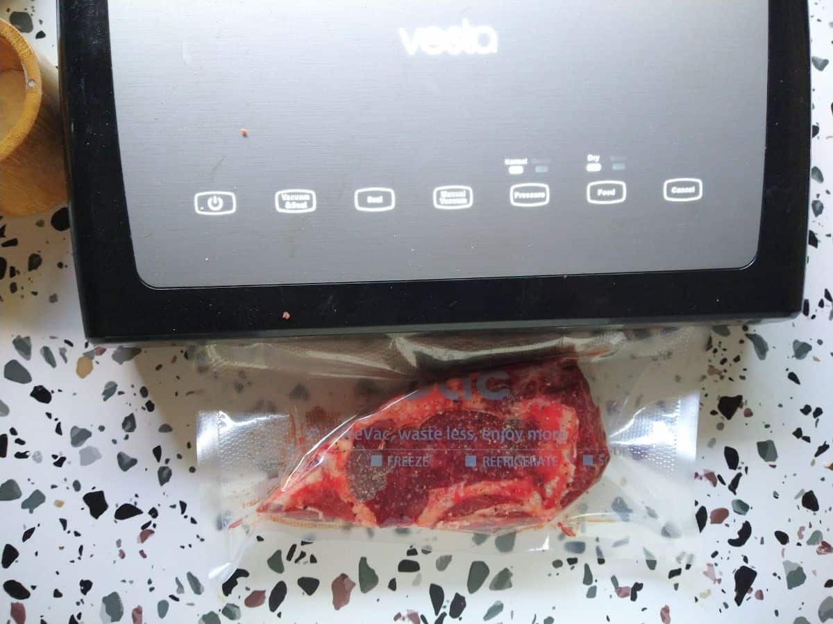 Vesta Vacuum Sealer shown sealing a bison ribeye steak on a white table with spots. 