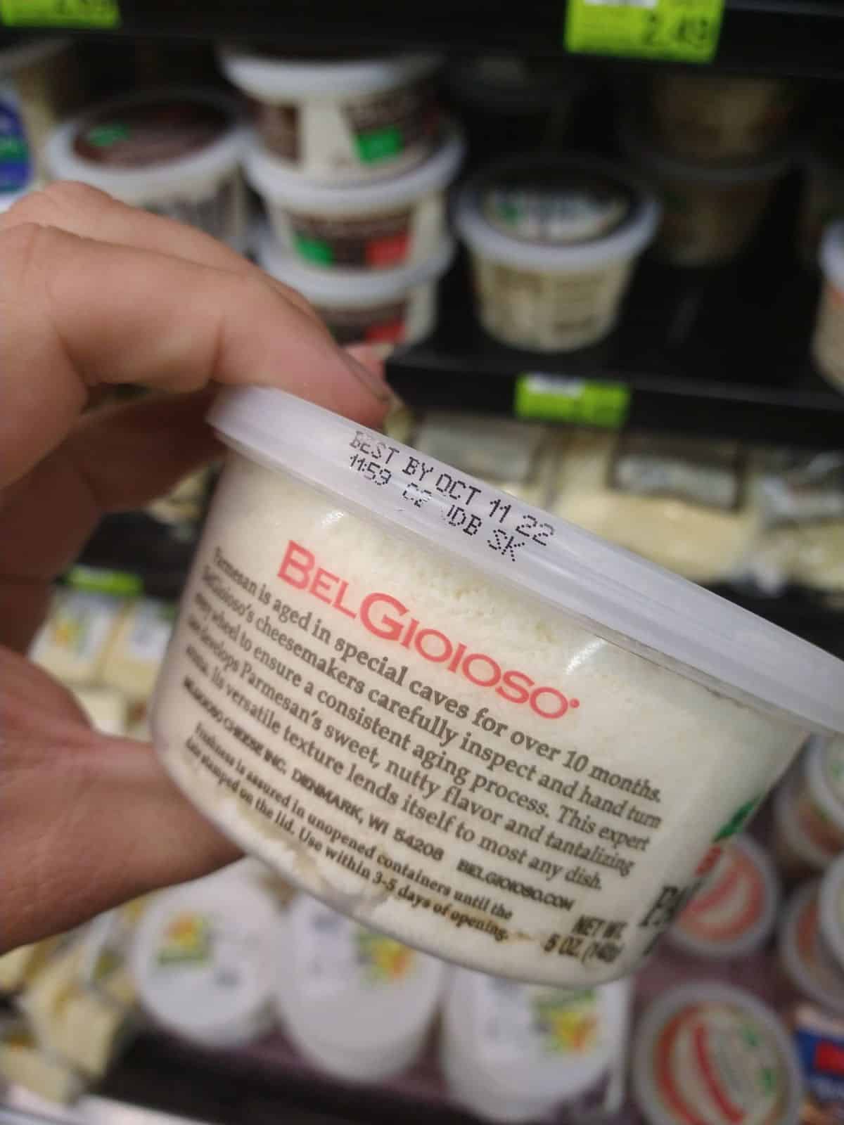 A container of BelGioIoso grated parmesan cheese is being held at the grocery store.