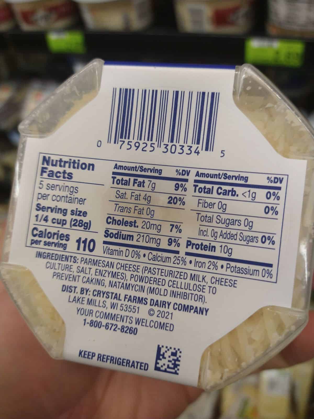 The back of a container of Crystal Farms shredded parmesan cheese is being held at the grocery store. The ingredients include Parmesan cheese, powdered cellulose to prevent caking, and natamycin (mold inhibitor). 
