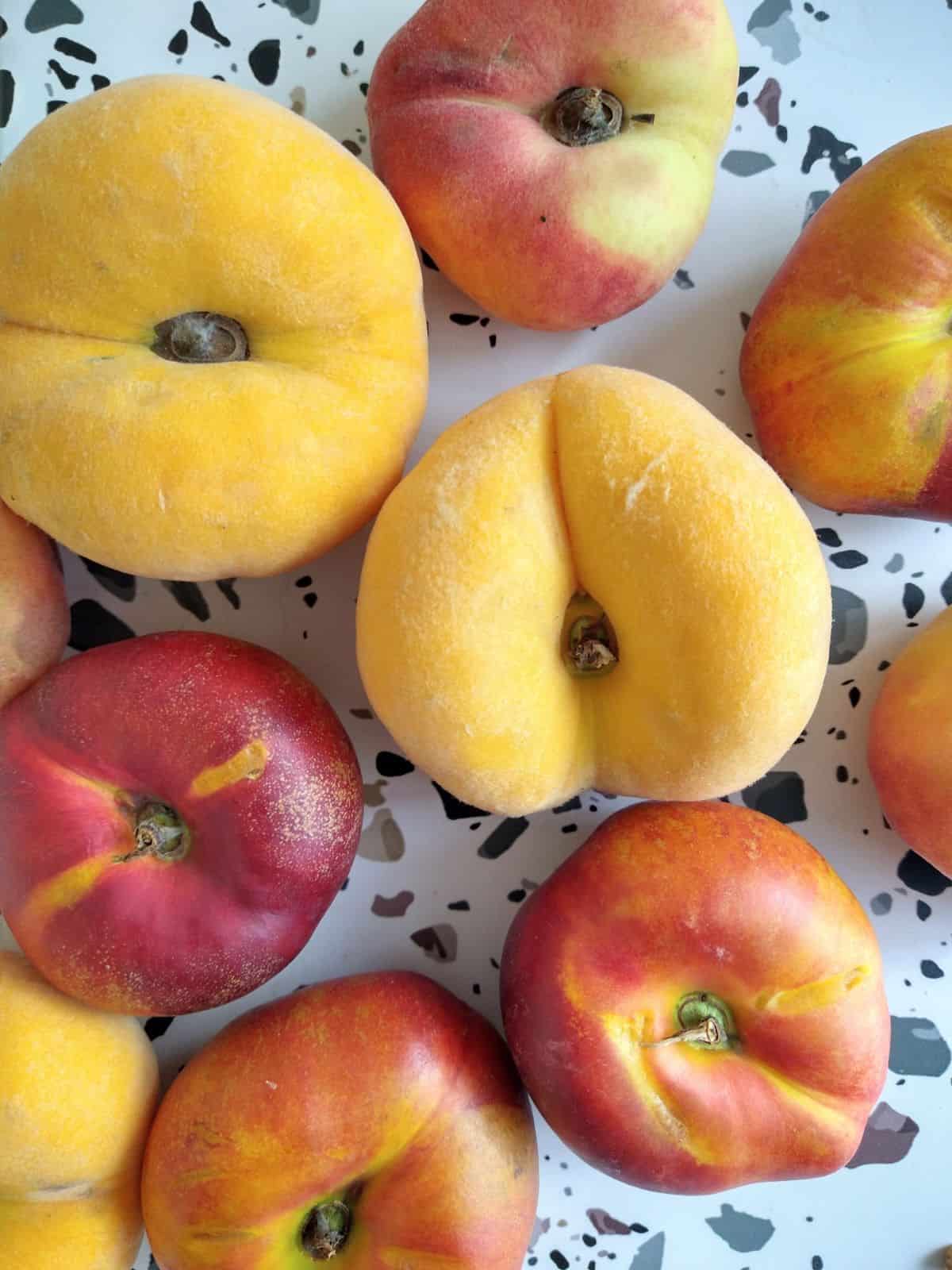 3 different types of Donut peaches and nectarine on a white table with colored dots.