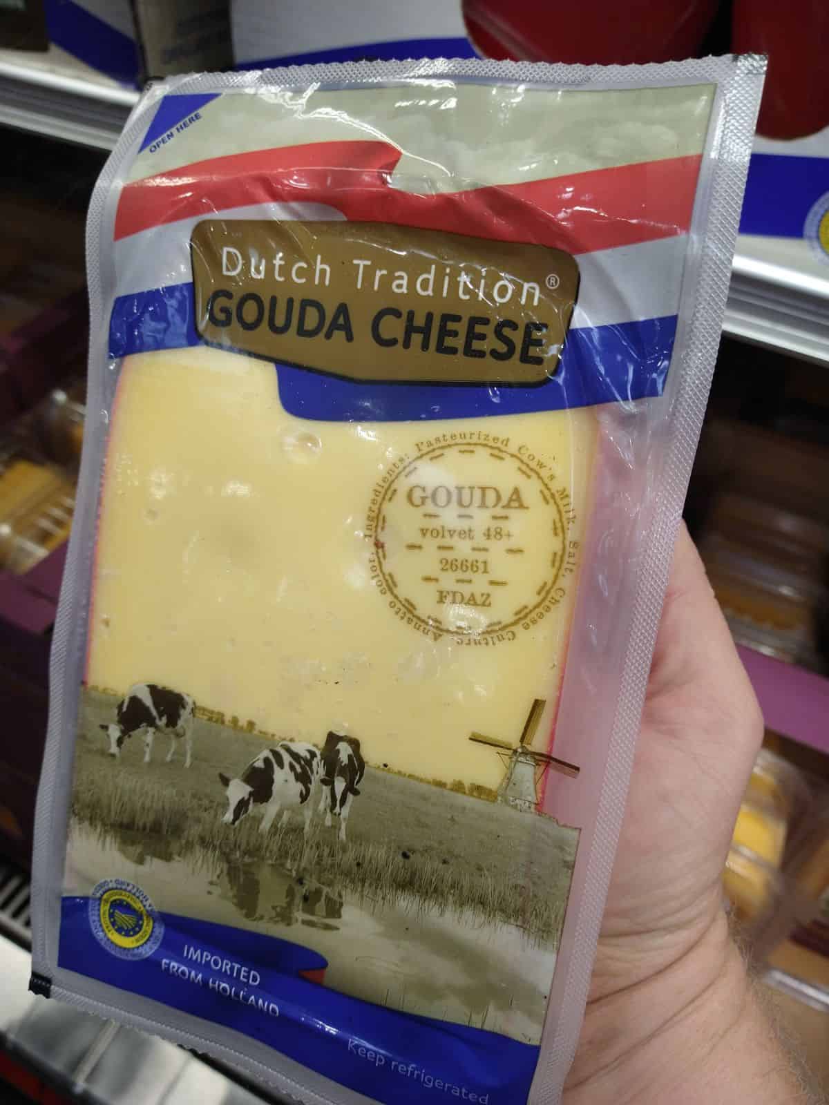 A large chunk Dutch Tradition Gouda Cheese is being held up.