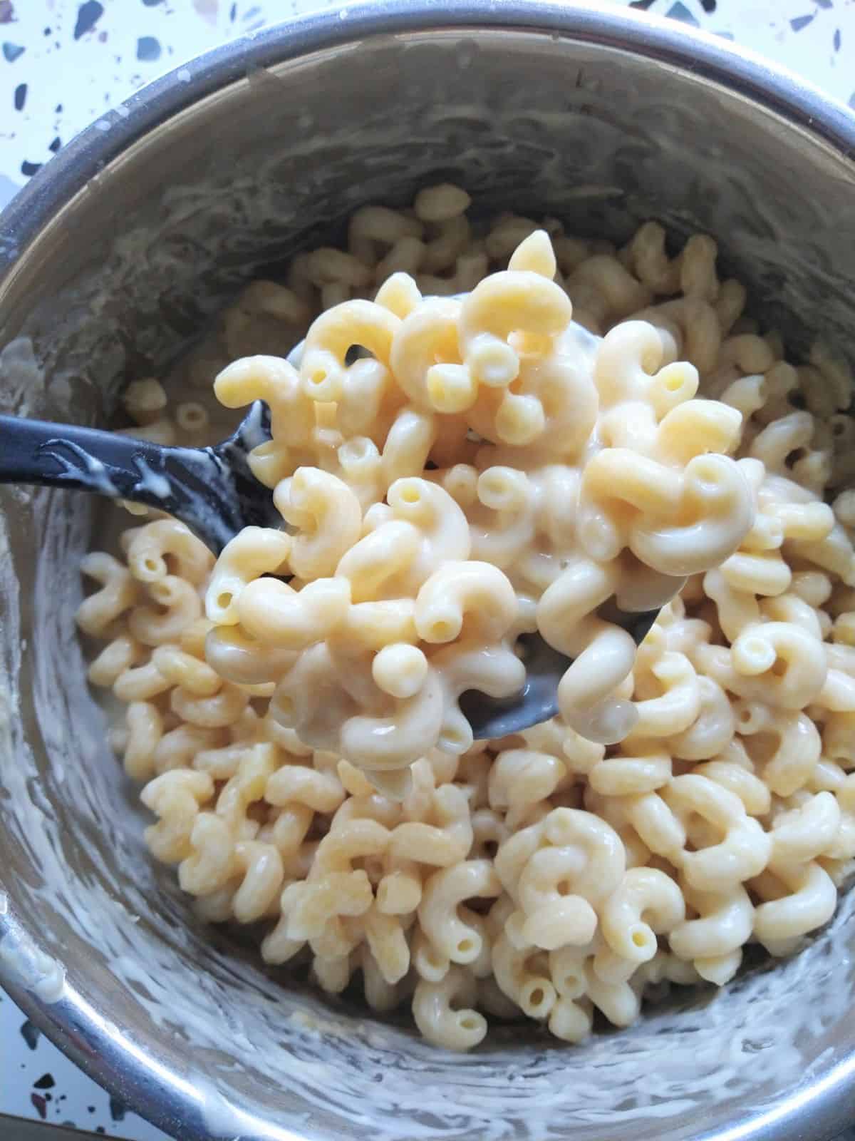 A spoon full of mac & cheese made with Butterkase cheese. The spoon is being held above the pot of mac & cheese.