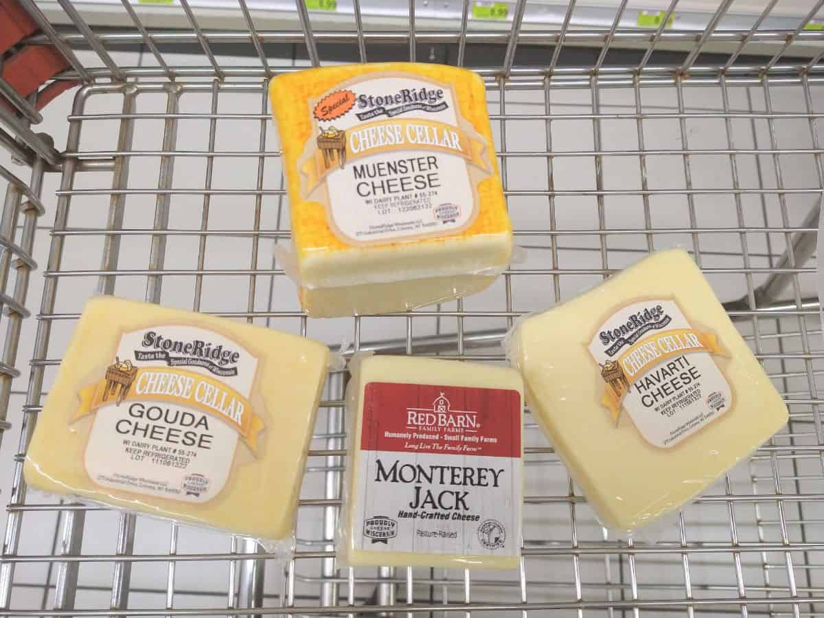 A metal grocery cart with Muenster cheese along with Gouda, Monterey Jack, and Havarti. 
