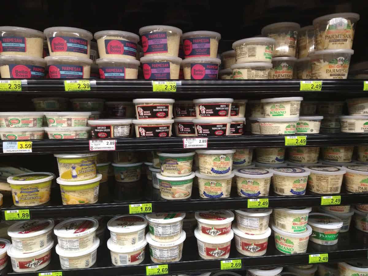 A grocery store display of containers of different types of Parmesan cheese.