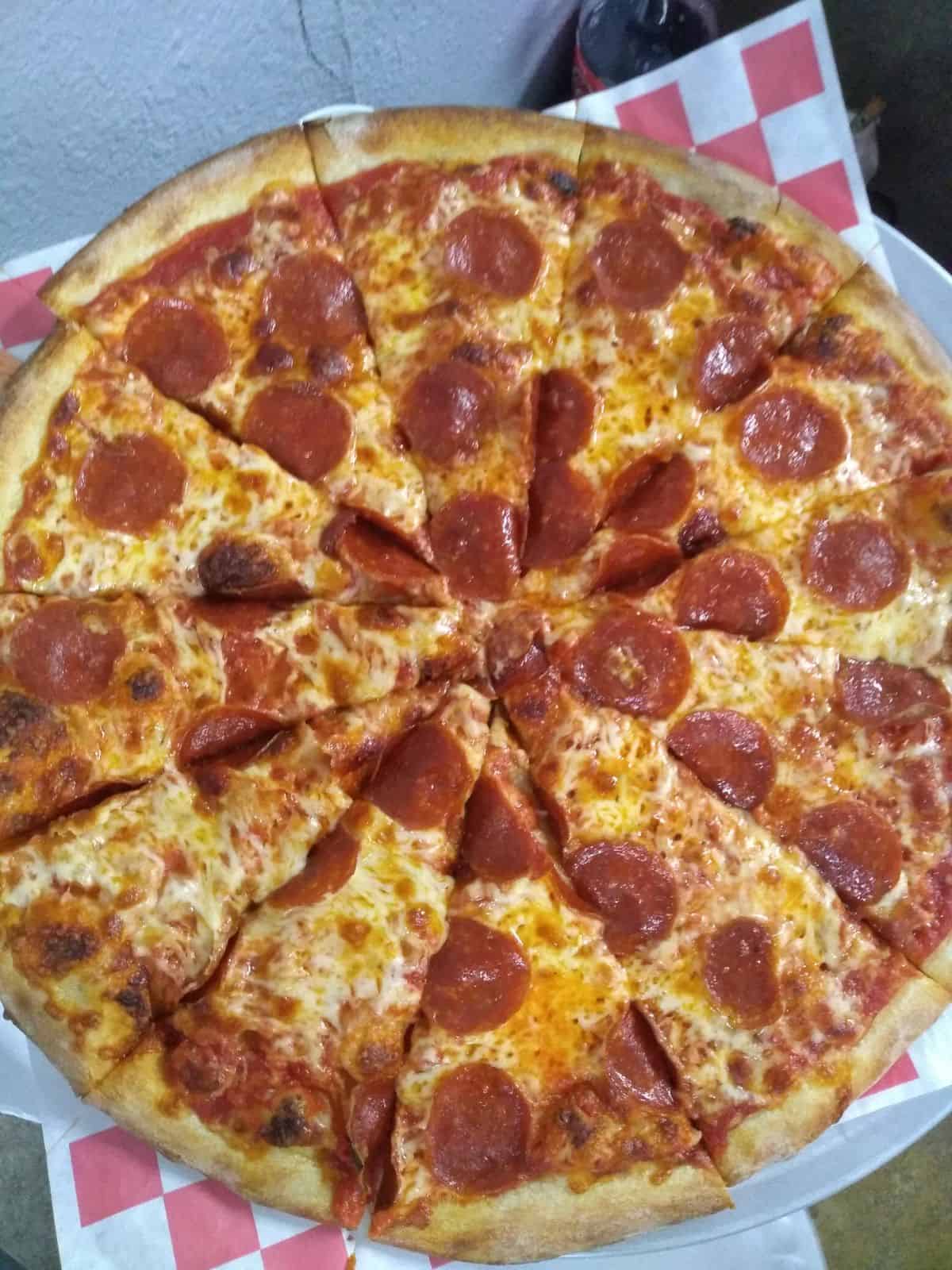 A pepperoni pizza on a metal pan with white paper with red squares underneath.