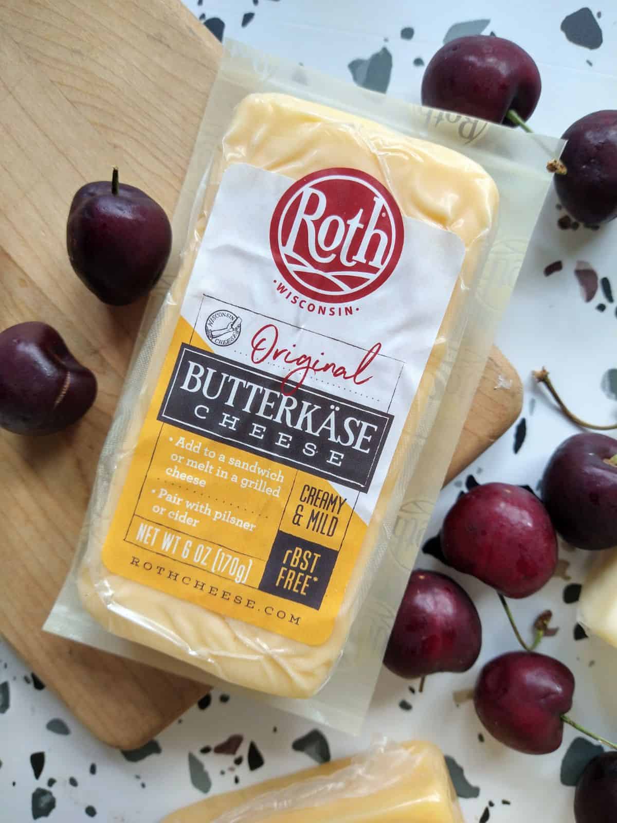 A chunk of Roth Butterkase cheese sitting on a small wood cutting board surrounded by fresh cherries. 