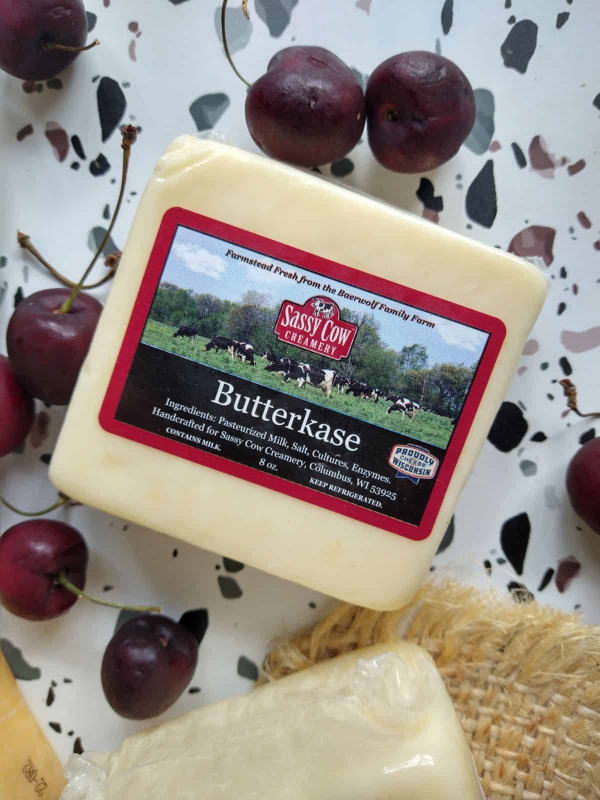 Sassy Cow Creamery Butterkase cheese sitting on a white table with spots along with fresh dark red cherries.