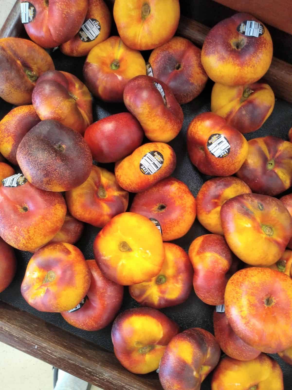 A wood display at a grocery store filled with flat yellow fleshed donut nectarines.