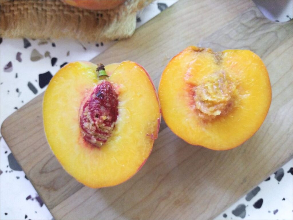 A cut in half freestone peach next to a clingstone peach on a cutting board.