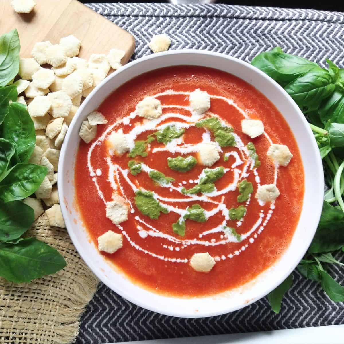 A bowl of tomato soup with cream and pesto and oyster crackers on top.