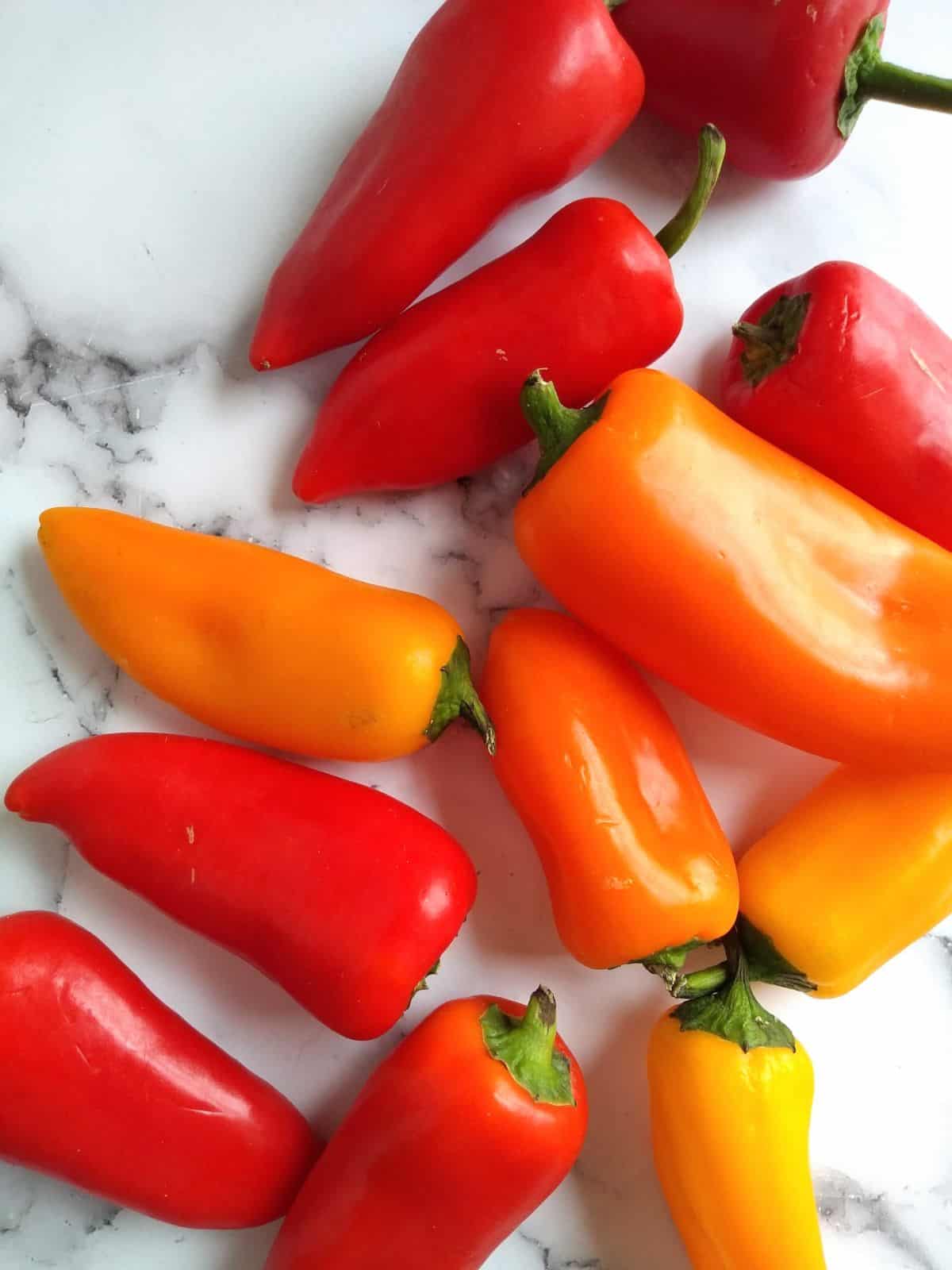 Orange and red mini peppers on a white with black surface.