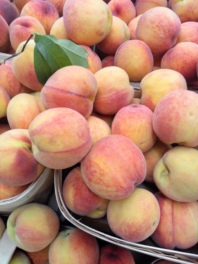 A close up of peaches that are overflowing half bushel baskets of fruit.