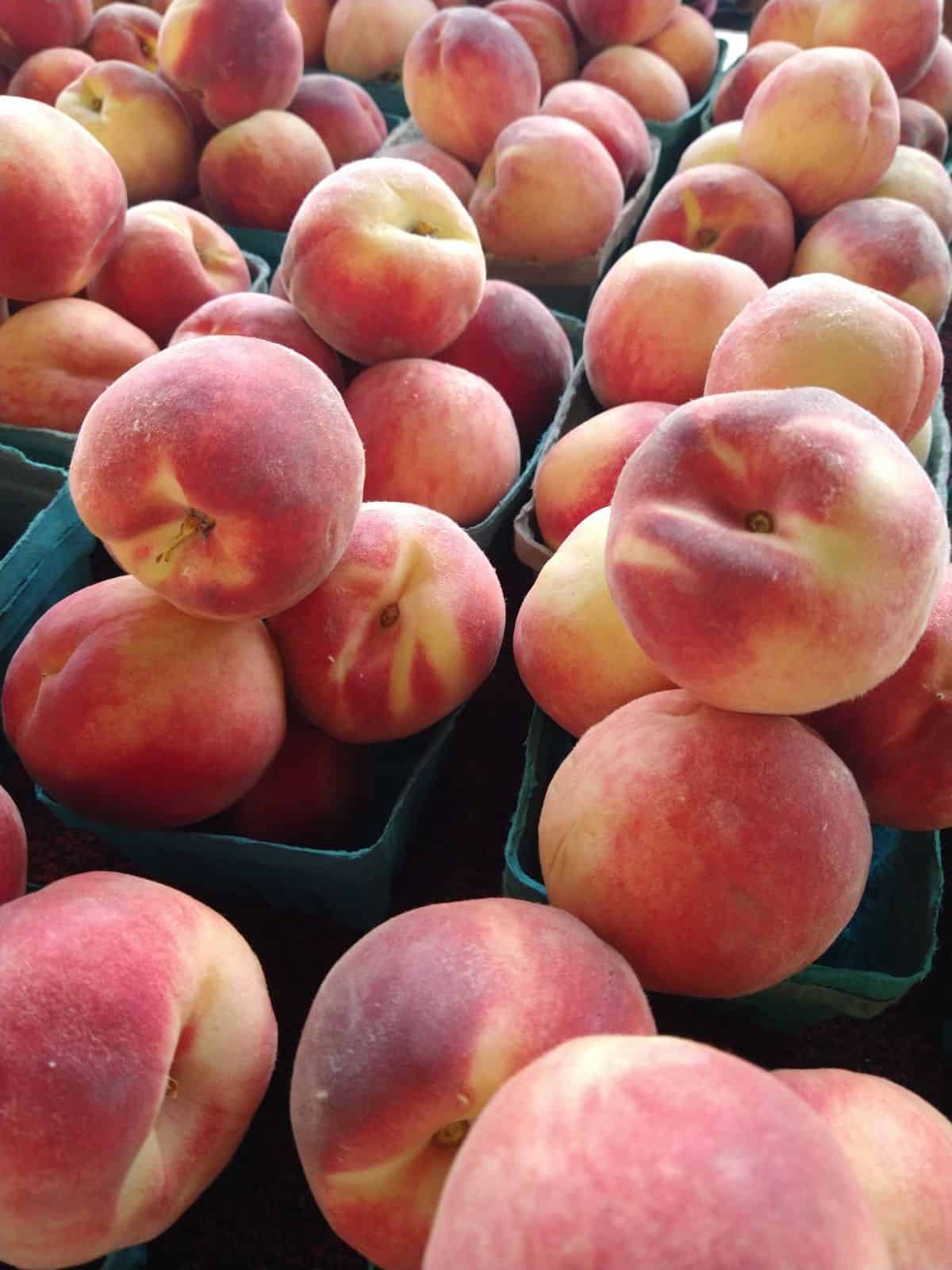 A display of white peaches in quart containers a the farmers market.