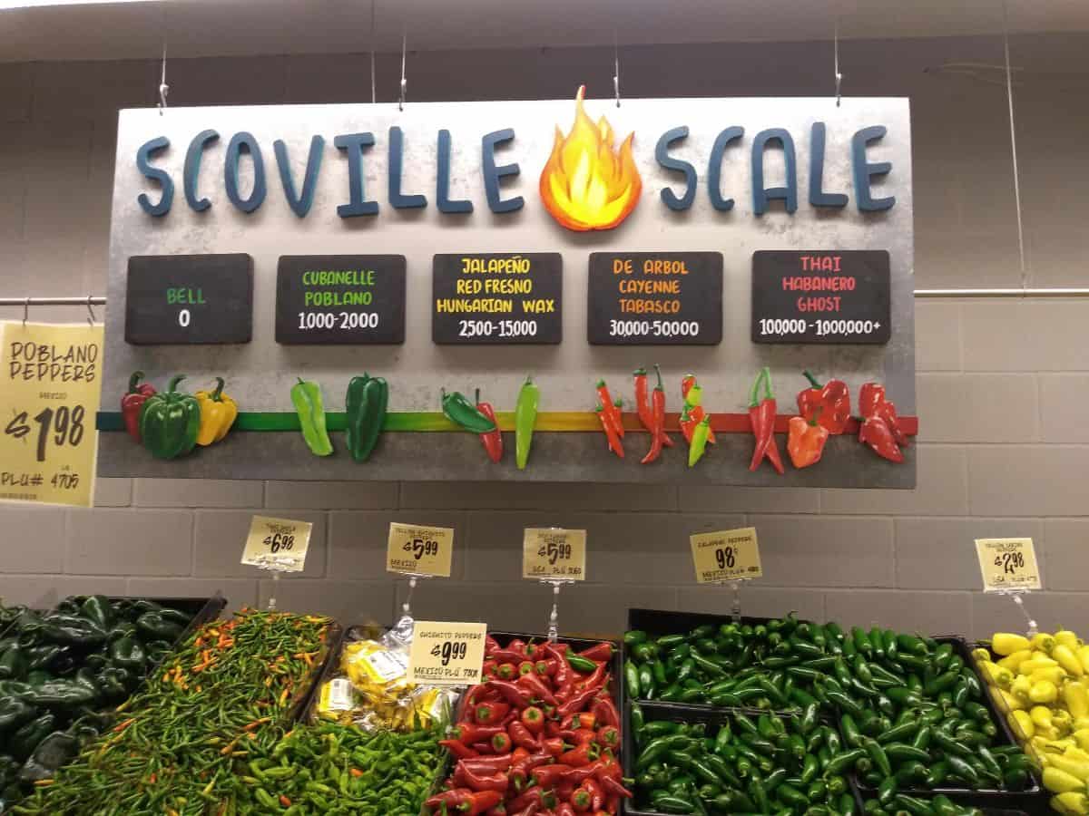 A Scoville Scale sign at a Central Market store in Fort Worth, TX. Under the sign is a big display of different types of peppers.
