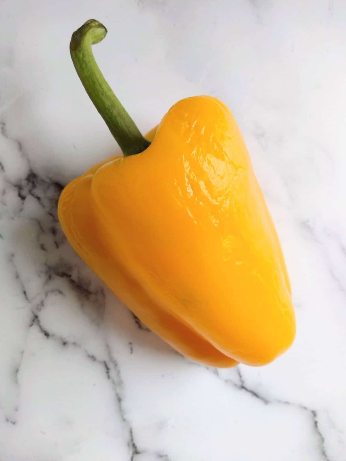 A single yellow bell pepper with shriveled skin on a white background