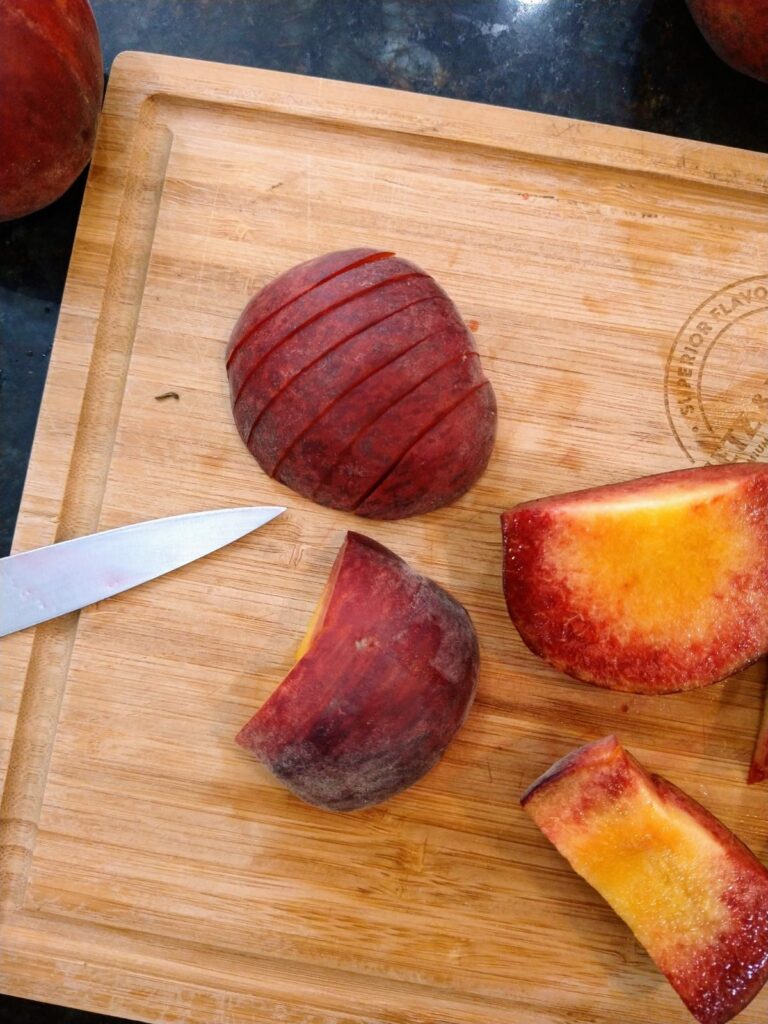 Peaches being sliced up for a peach pie are sitting on a wood cutting board. The slices are not peeled.