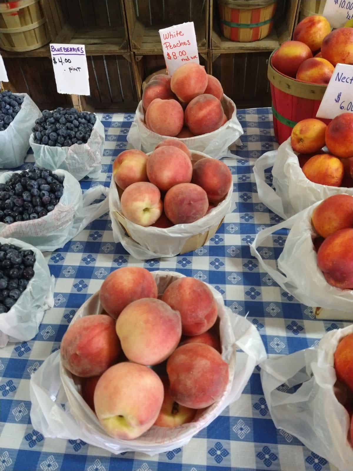 A display at an orchard featuring blueberries, white peaches, and nectarines on a table with a blue plaid cloth. 