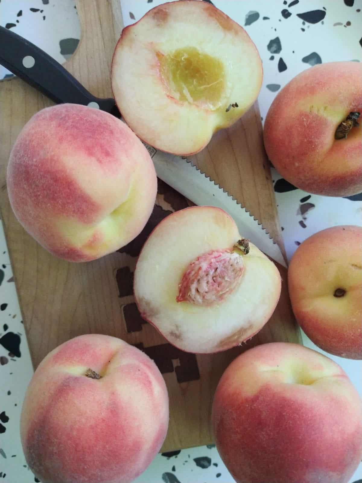 A wood cutting board with white flesh peaches cut open on it. 