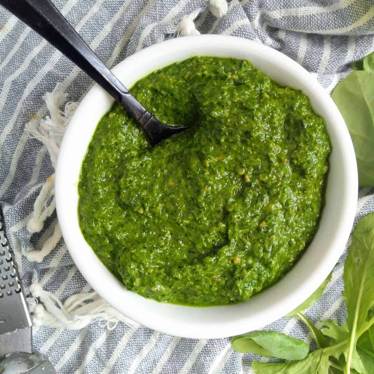 A white bowl filled with spinach pesto with arugula. 