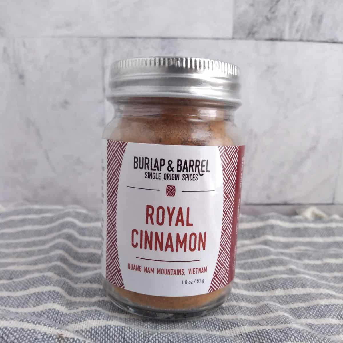 A jar of Burlap & Barrel Royal Cinnamon on a towel in front of a tile background.