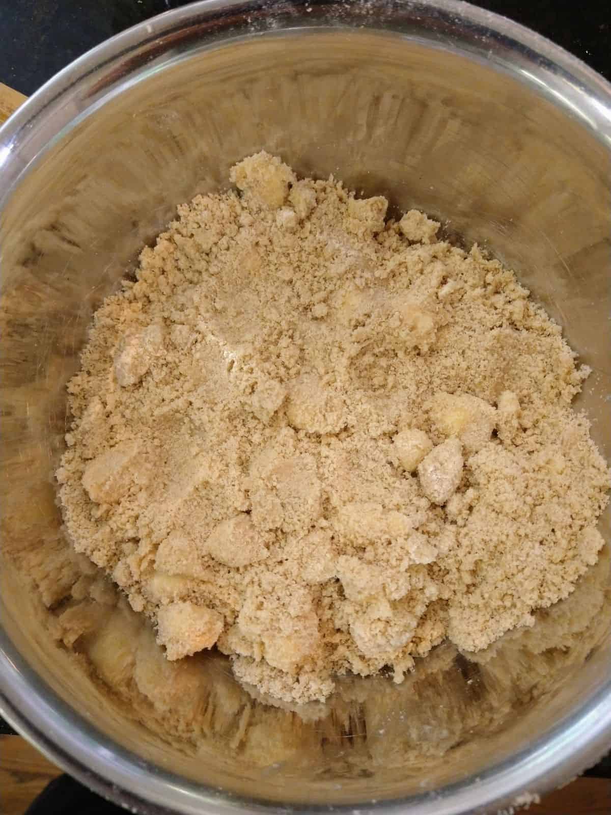 A brown sugar, flour, and butter crumble topping inside a large metal mixing bowl.