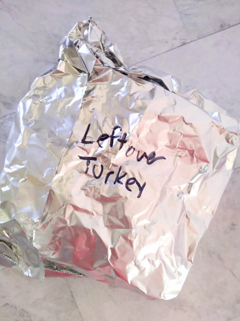 Turkey that is wrapped up in foil with the words "Leftover turkey" written in black marker on the outside.