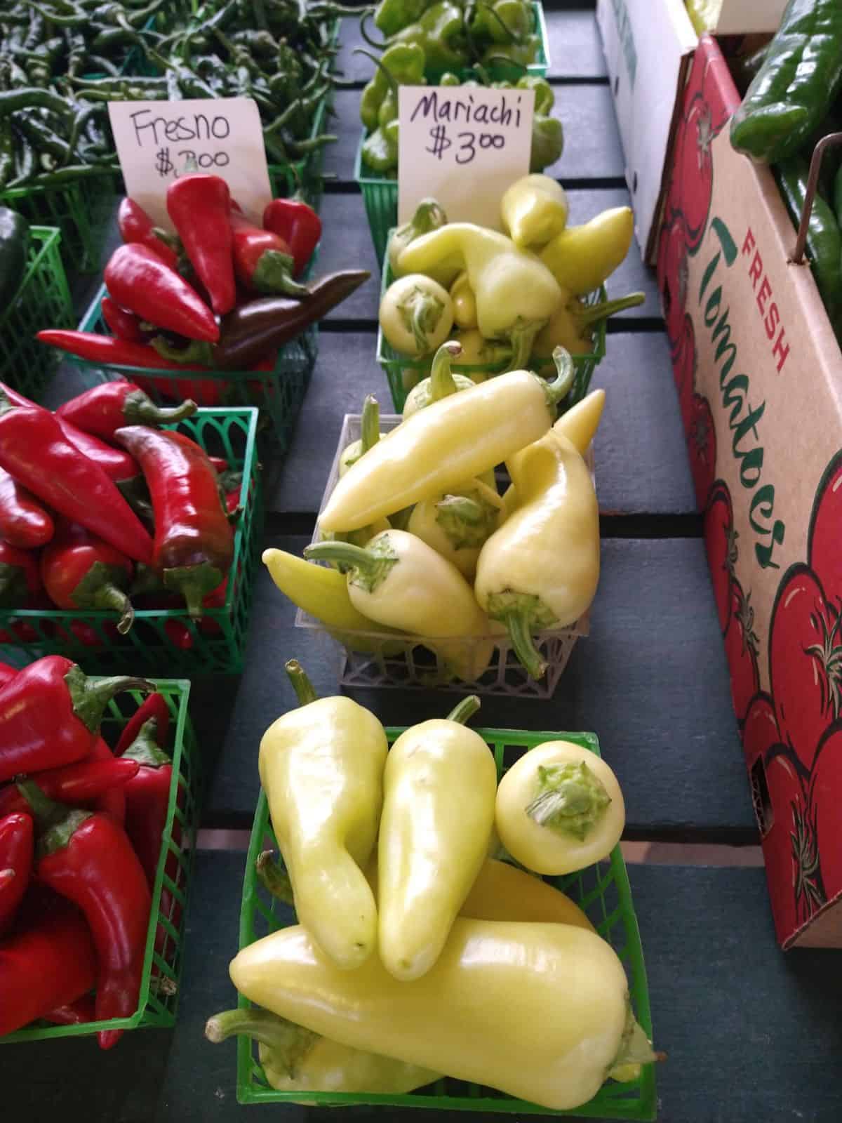 A farmers market table with baskets of Fresno and Mariachi peppers. 