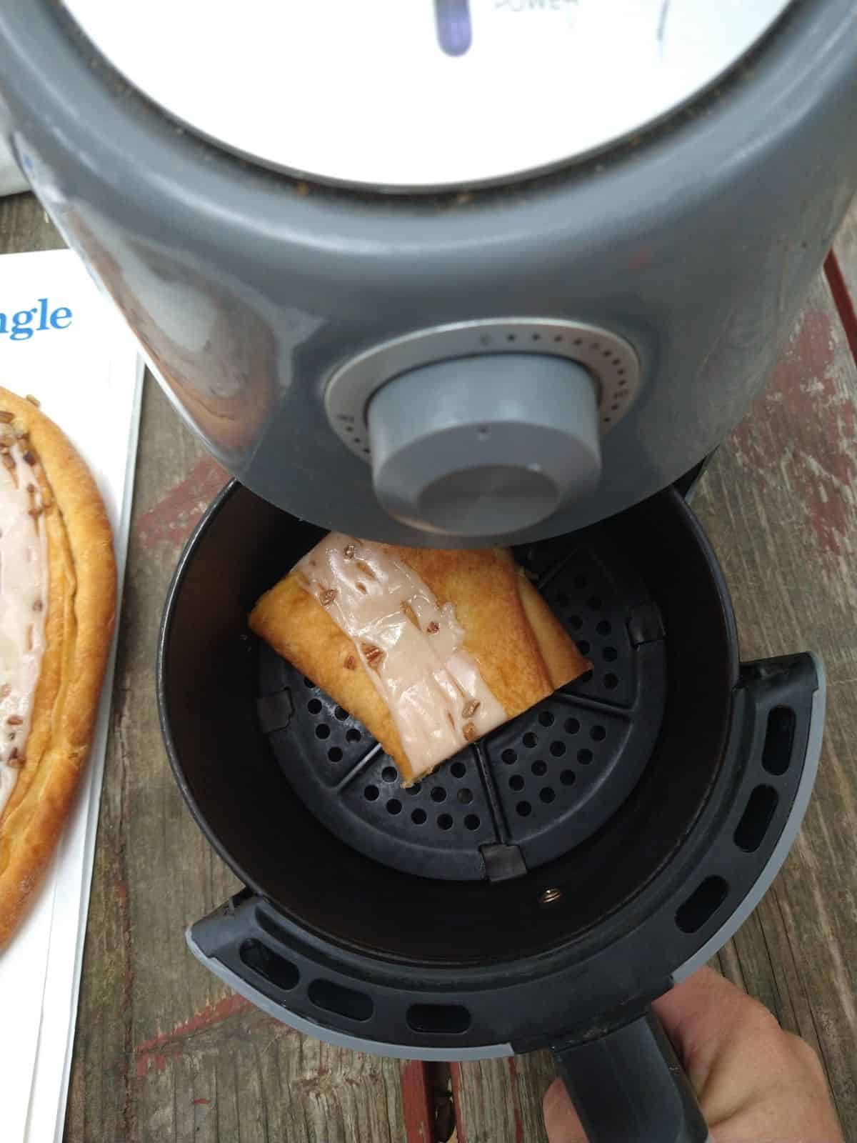 An air fryer opened up with a slice of Danish Kringle going in. 