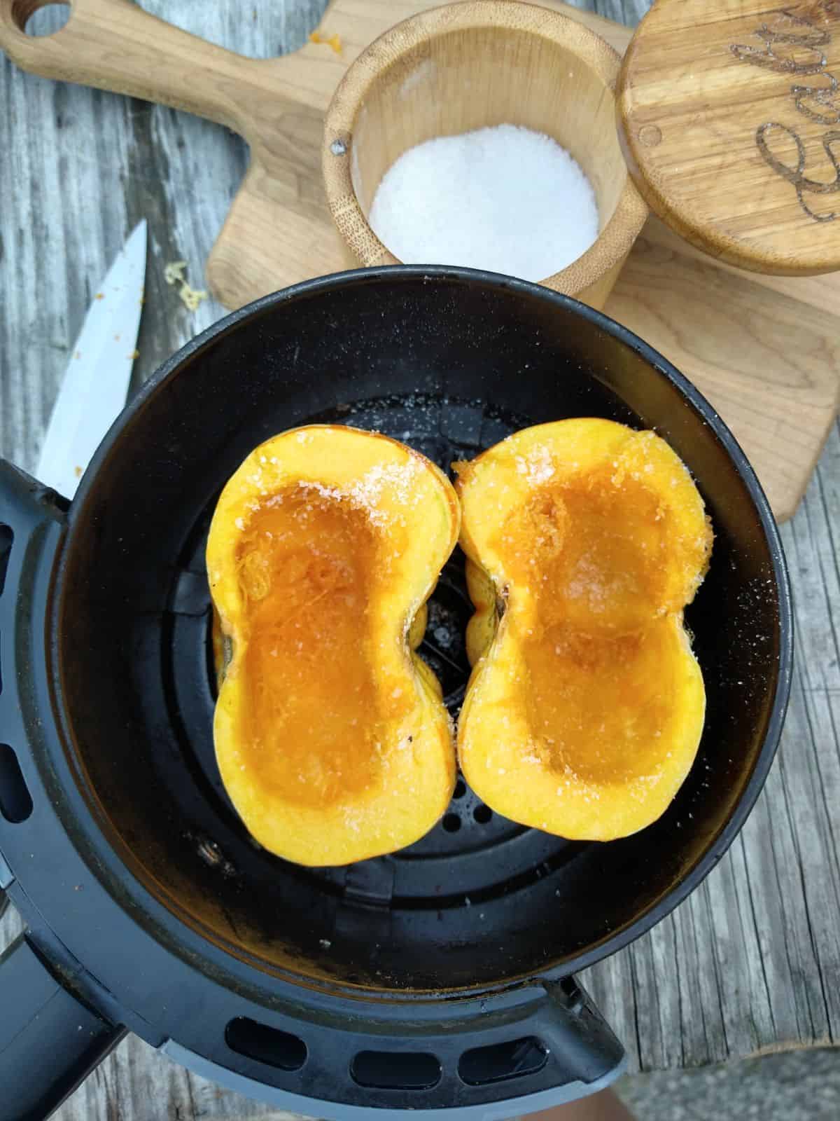 Two halves of a Tiger Strip pumpkin that has been cut open and is inside the air fryer basket. Salt has been added to the halves. 