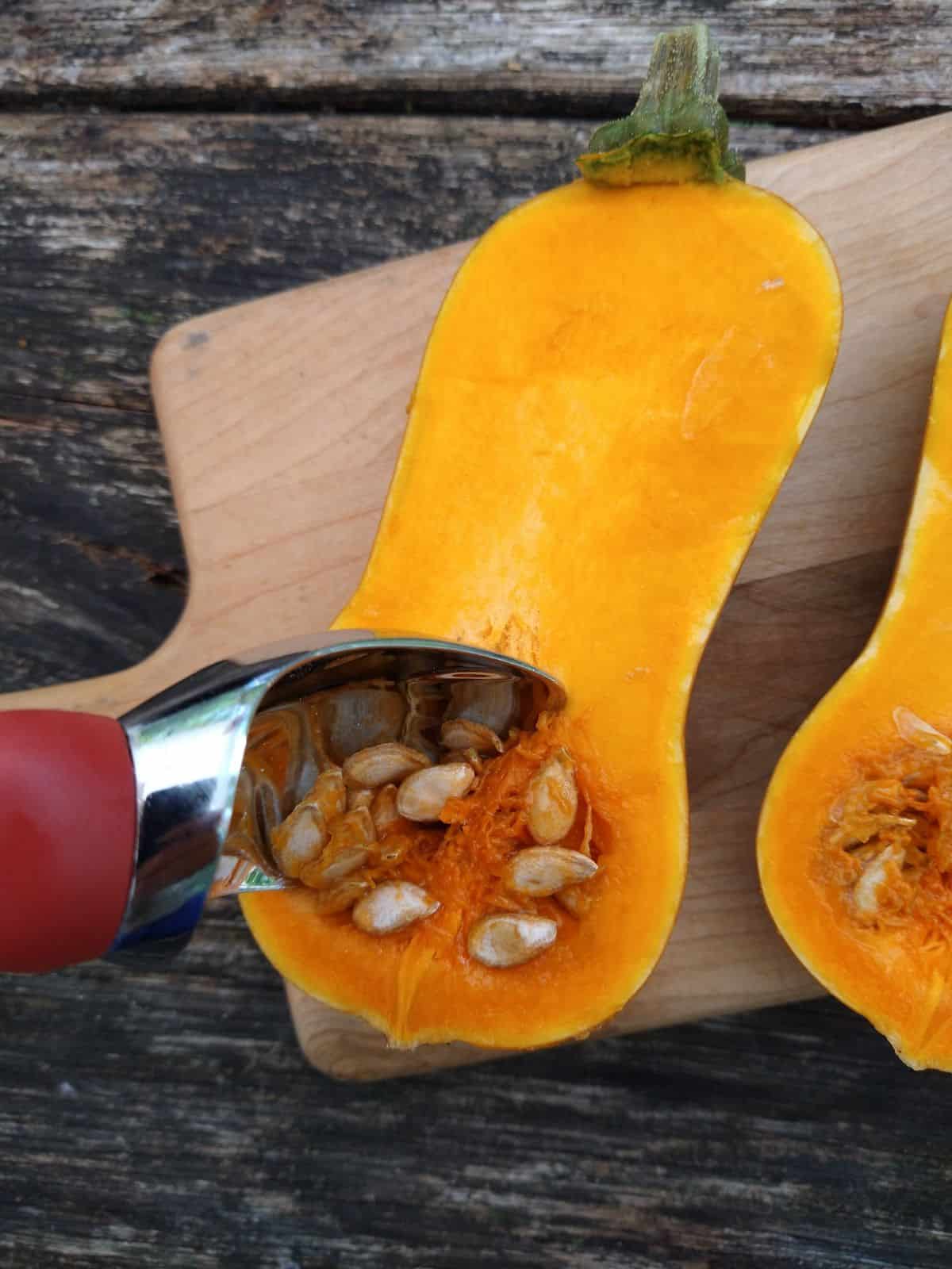 Two halves of a Honeynut squash getting the seeds scooped out with a ice cream scoop.