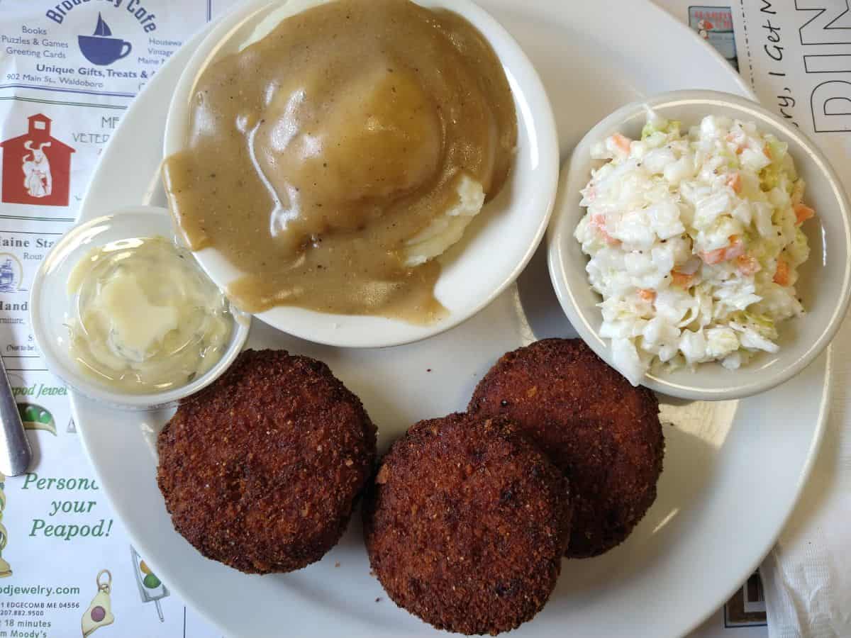 A plate of food of fish cakes, coleslaw, and mashed potatoes with gravy.