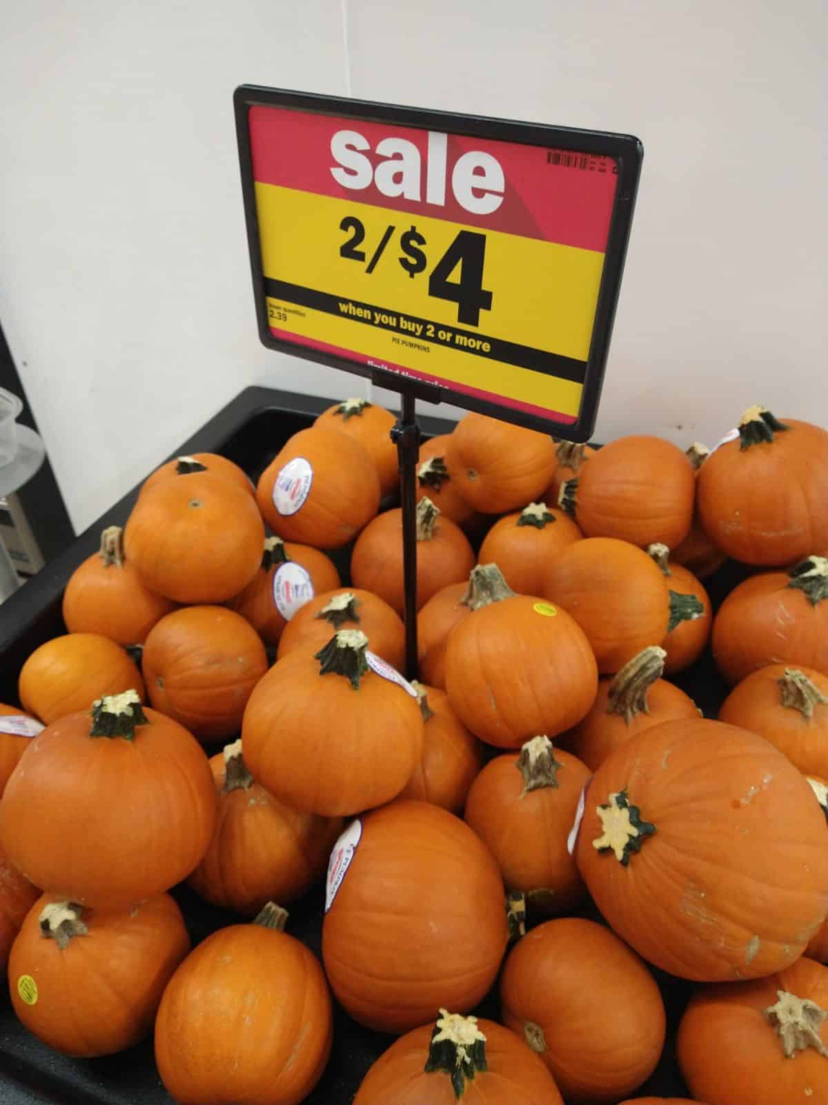 A display of pie pumpkins with a sale sign that says 2 for $4.
