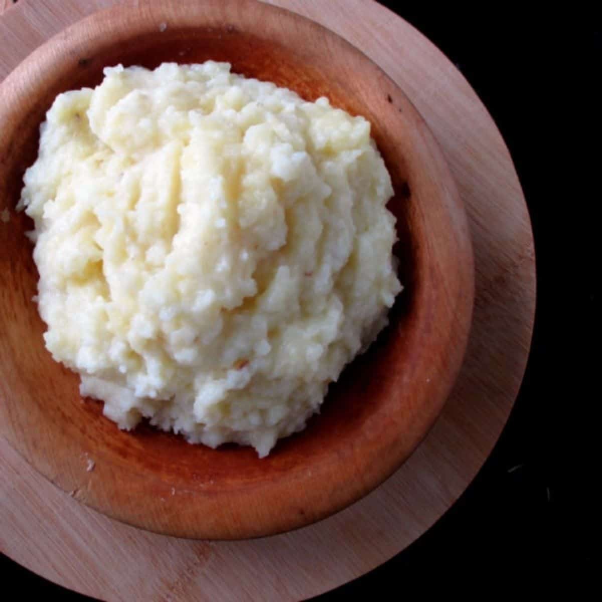 A wood bowl of whipped mashed potatoes sitting on a different colored wood board.