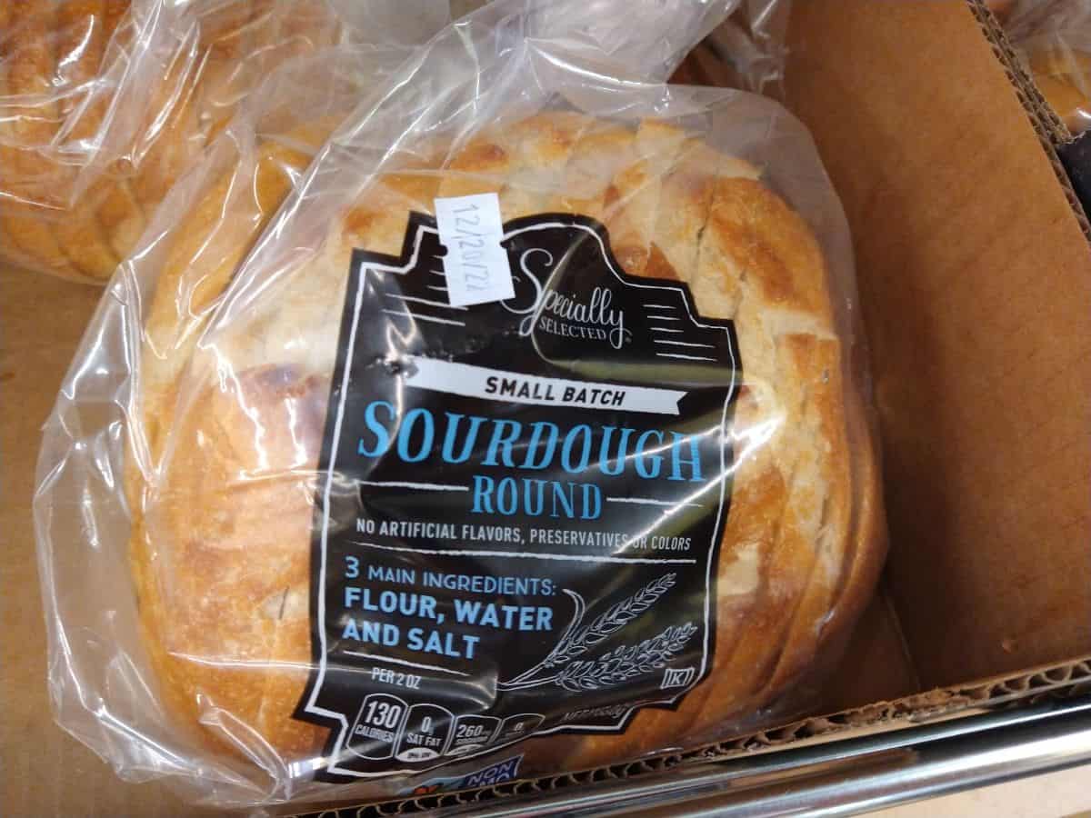 A loaf of Small Batch Sourdough Round in a clear plastic bag at a shelf in ALDI.