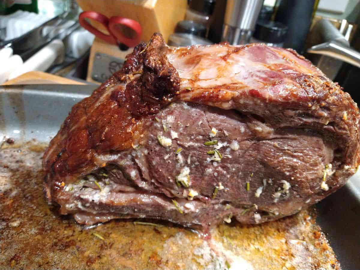 A finished standing rib roast covered in herb butter sitting in a sheet pan.