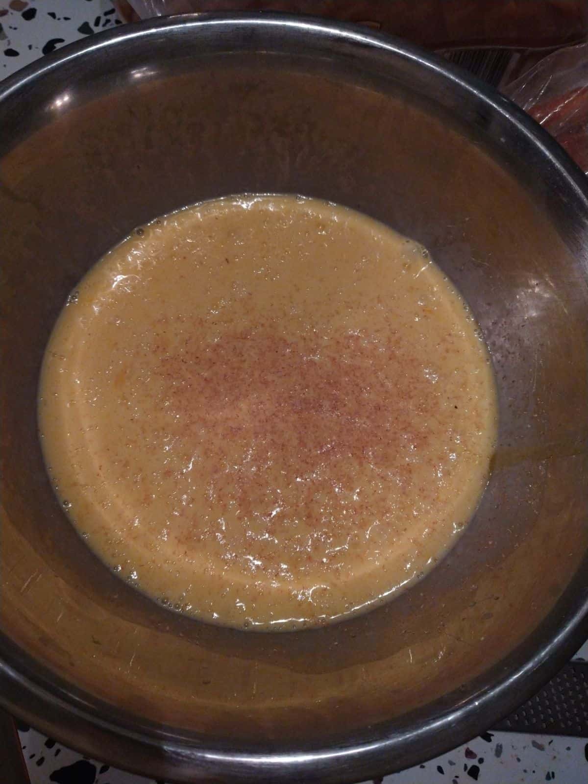 A mixing bowl filling with eggs, egg nog, and freshly grated nutmeg.