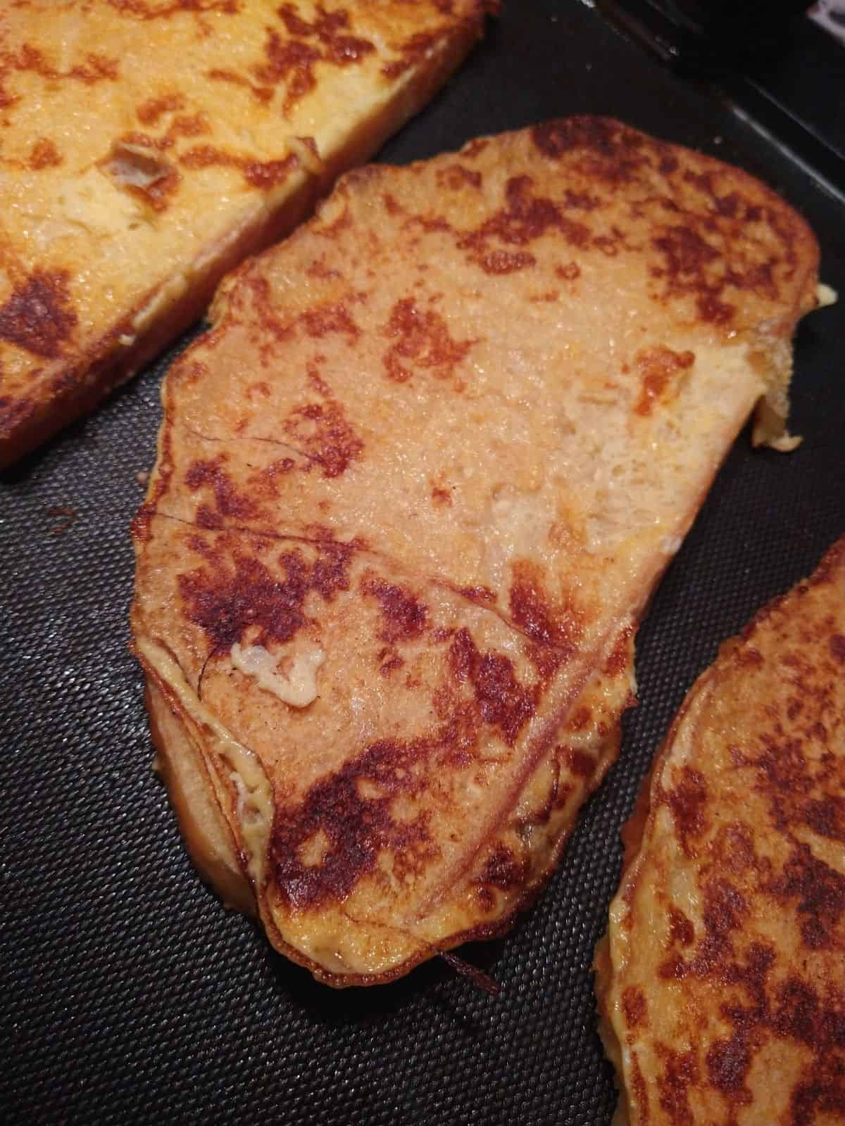 Finished slices of sourdough egg nog French toast on an electric griddle.
