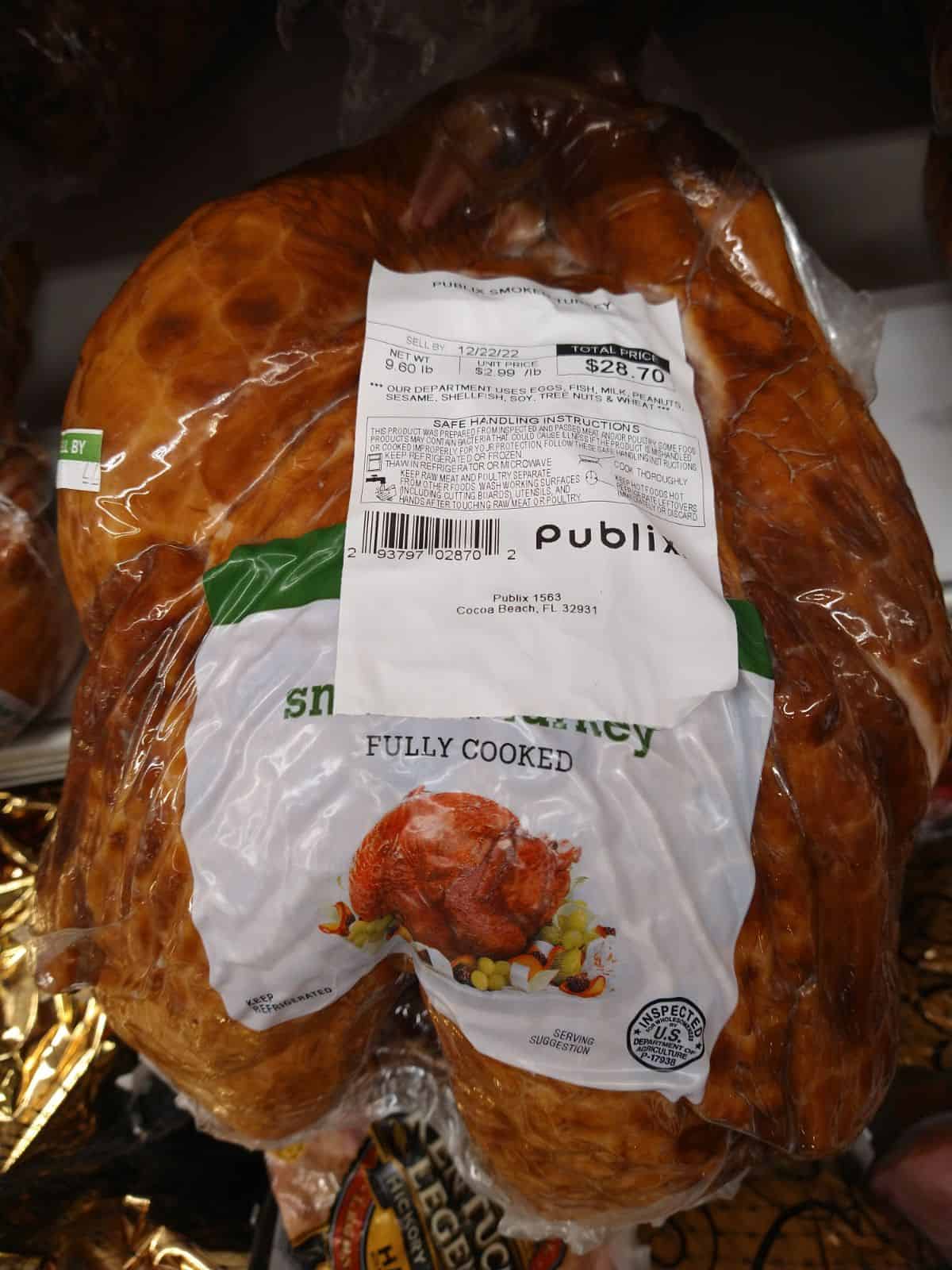 A Publix fully cooked smoked whole turkey in it's wrapping with a sticker showing that it's $2.99 a pound and costs $28.70.