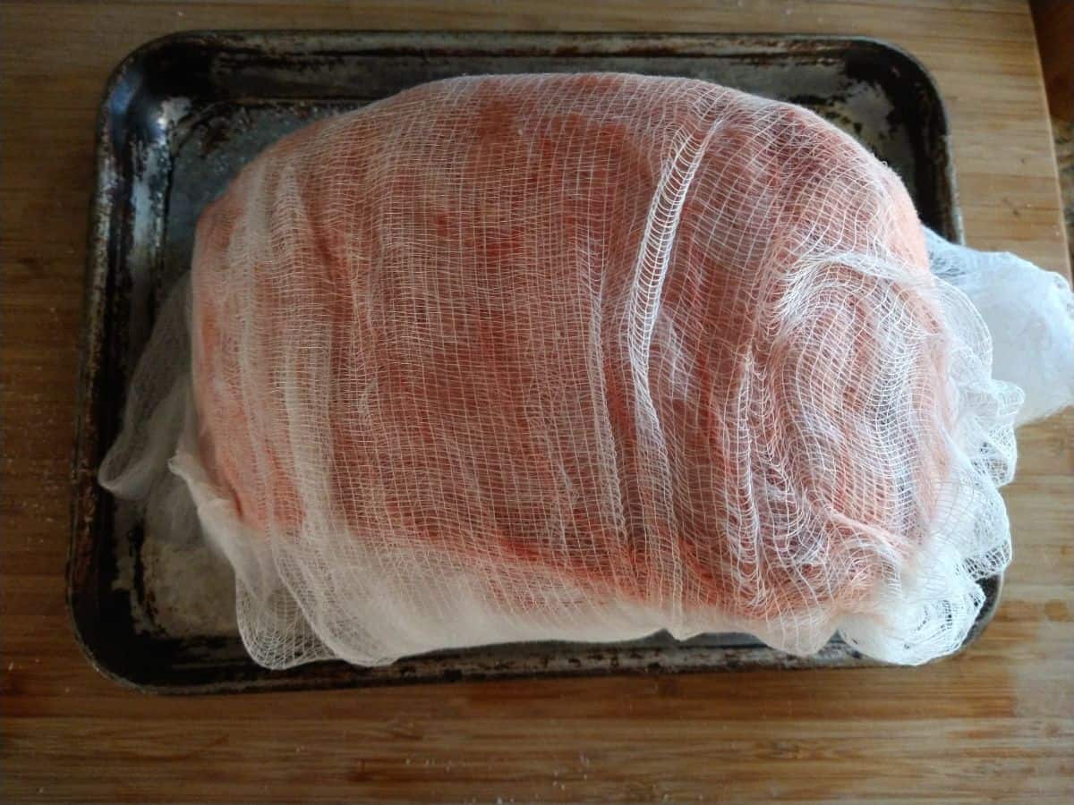 A standing rib roast wrapped in cheese cloth sitting on a sheet pan.