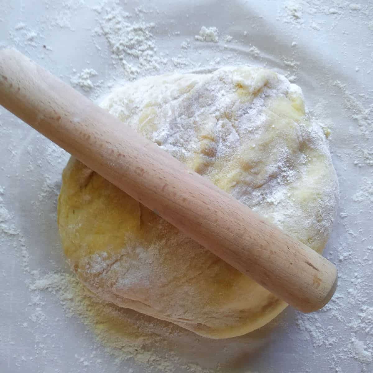 A small rolling pin on top of half of the dough that has been floured and placed on parchment paper.