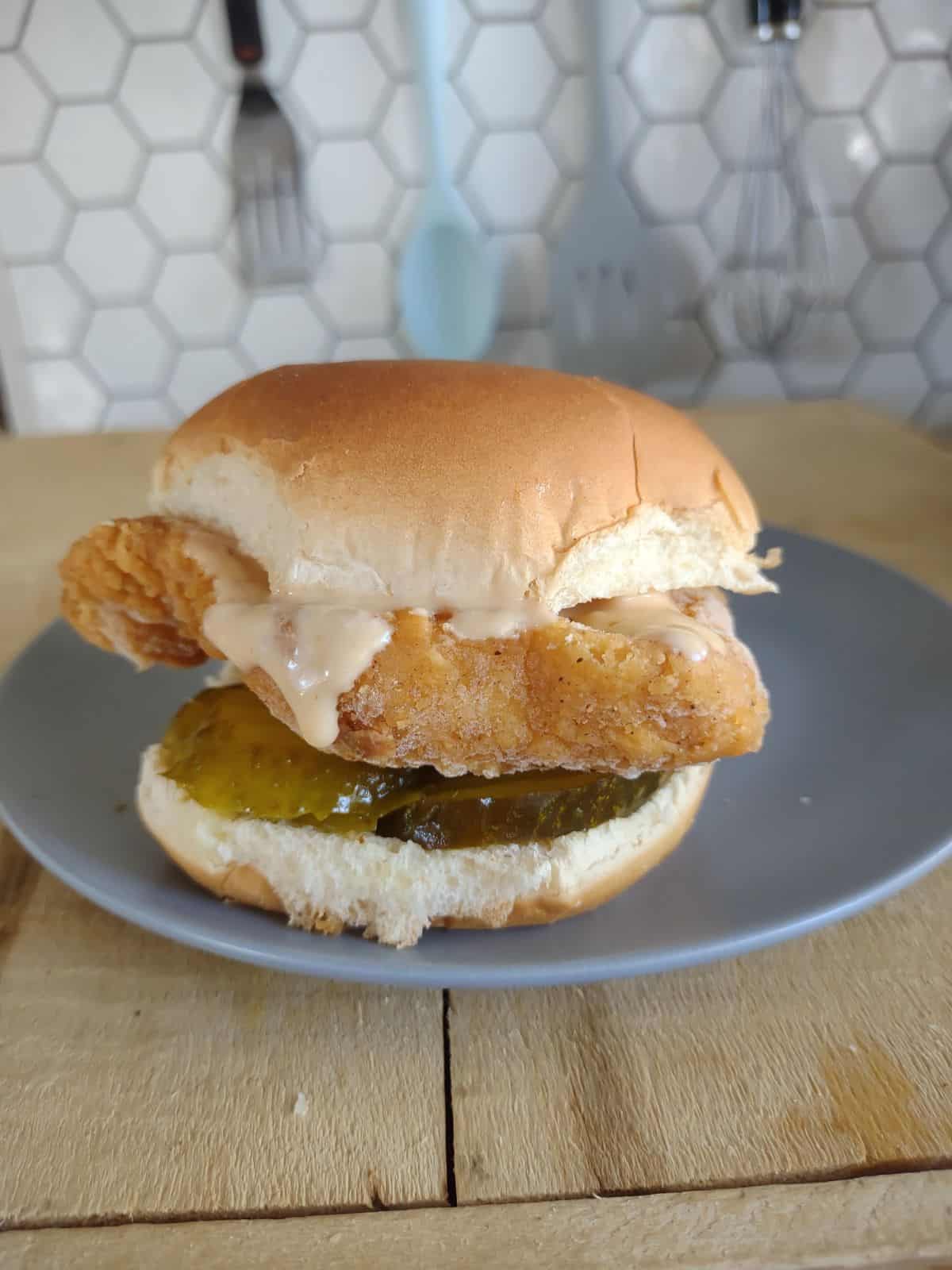 A side view of a copycat Chick Fil A Sandwich using ALDI ingredients. The sandwich has a chicken filet with a copycat Chick Fil-A sauce and pickles on bottom.