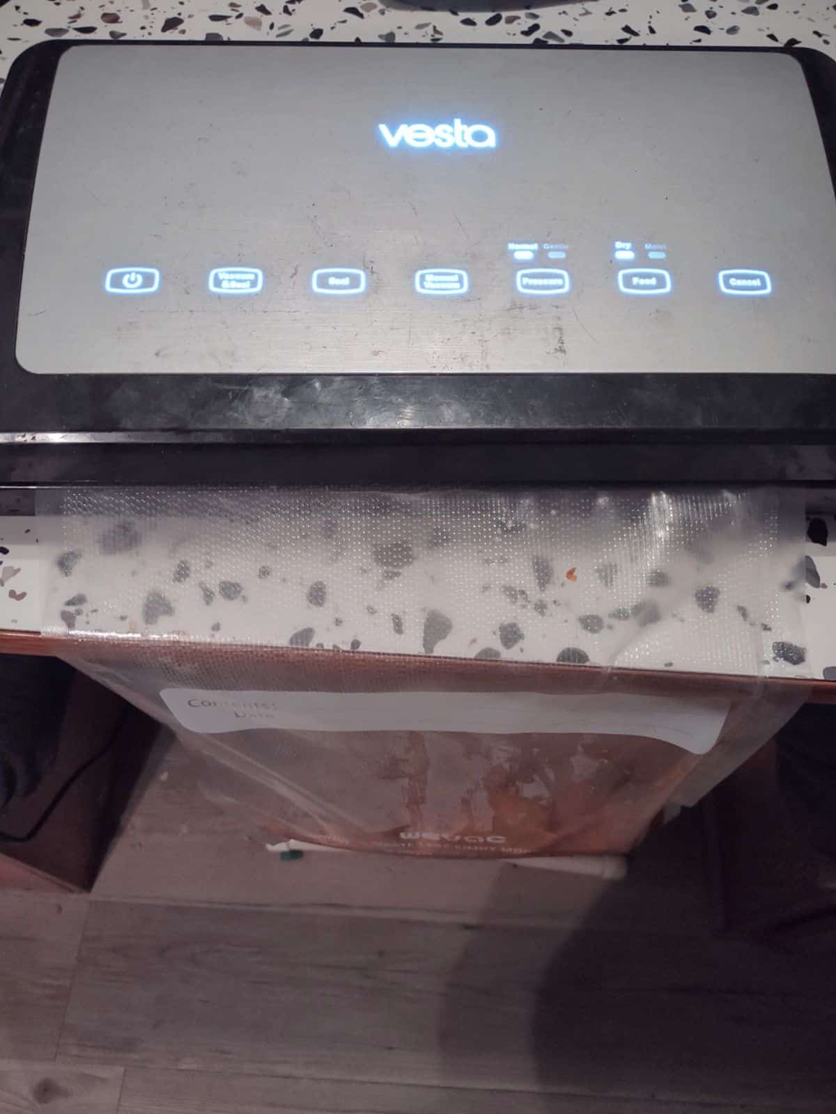 A bag looked into a vacuum sealer. The bag is hanging off the edge of a table 