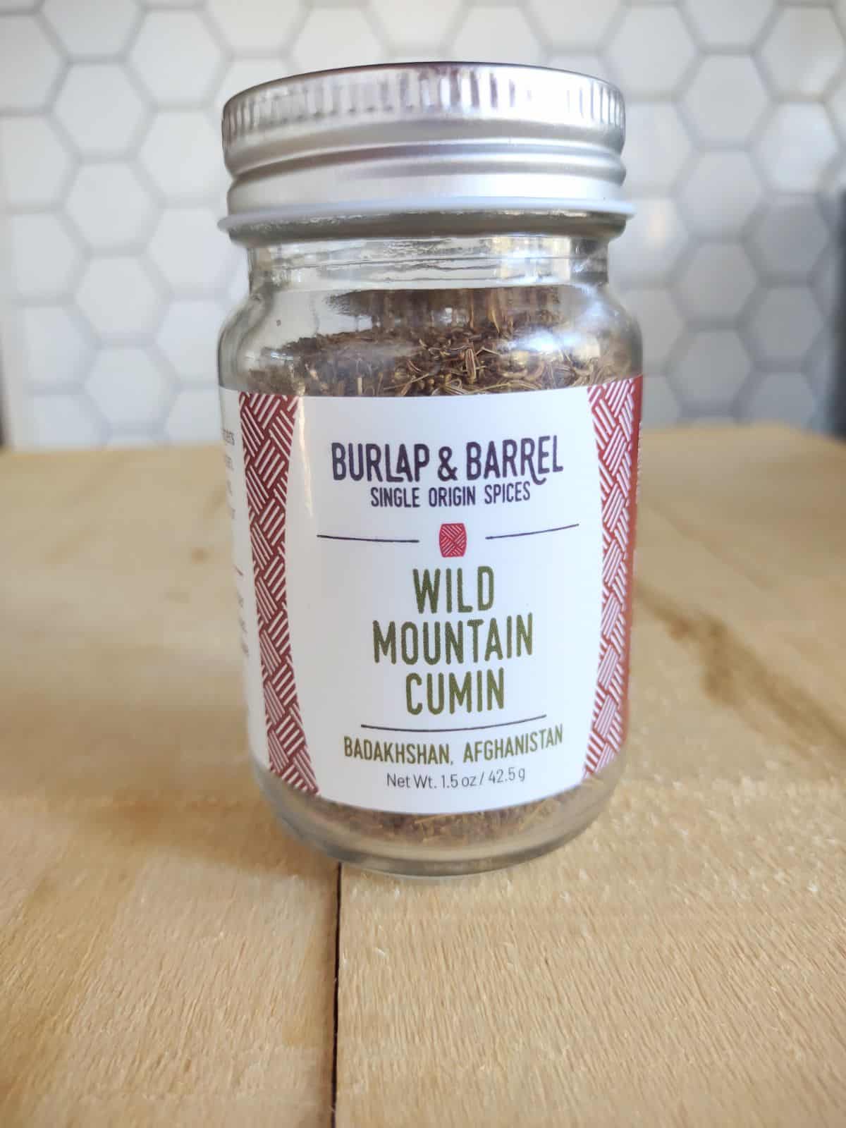 A jar of Burlap & Barrel Wild Mountain Cumin sitting on a wood board.