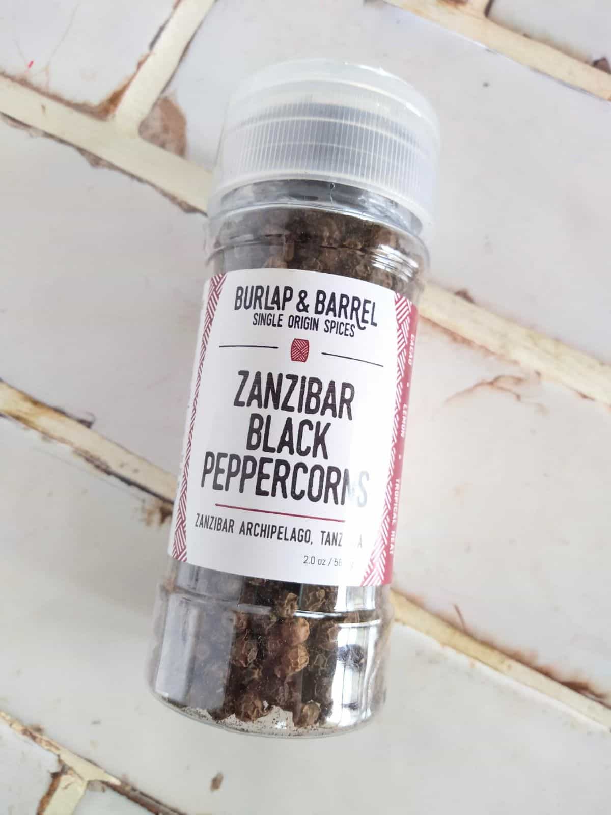 A grinder of Burlap & Barrel Zanzibar Black Peppercorns on a white tile countertop. This spice was featured on Shark Tank.