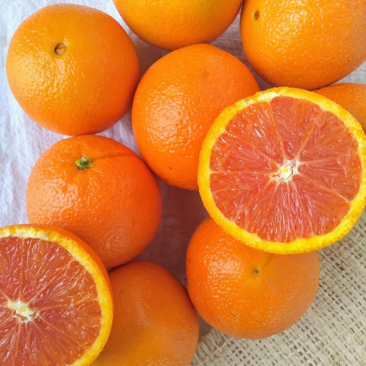 Cara Cara Navel oranges on a white towel with one orange cut open to show the red interior. 