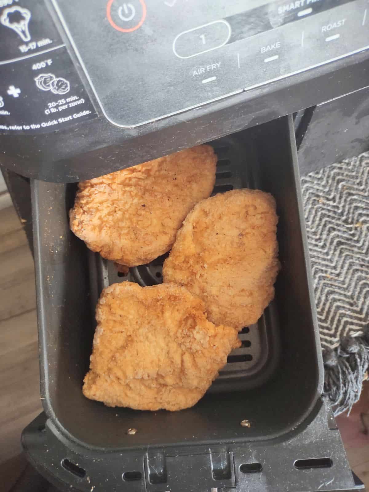 3 frozen red bag aldi chcken filets in an air fryer basket.