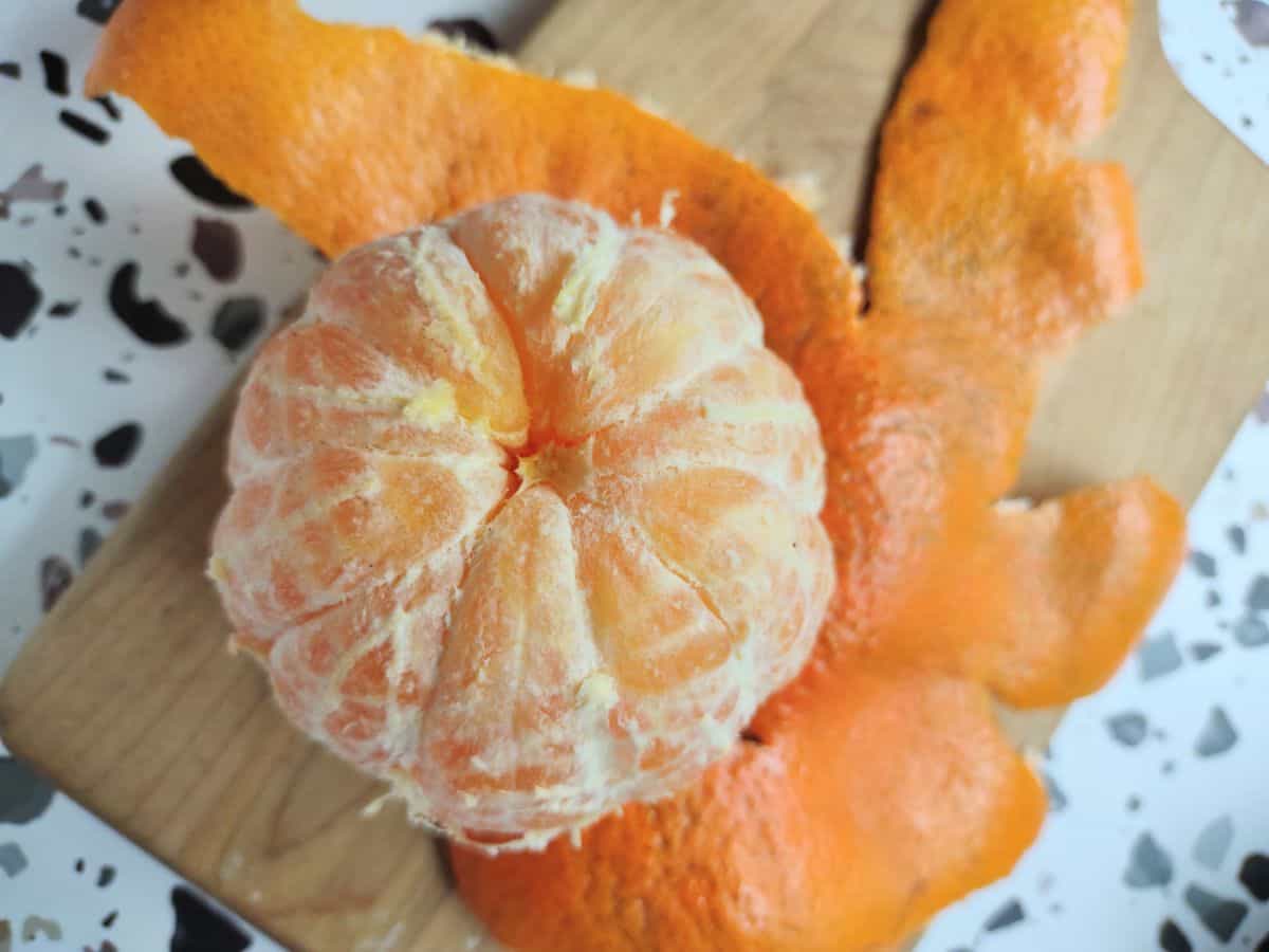 A peeled Juicy Crunch tangerine sitting on top of it's peel on a wood cutting board.