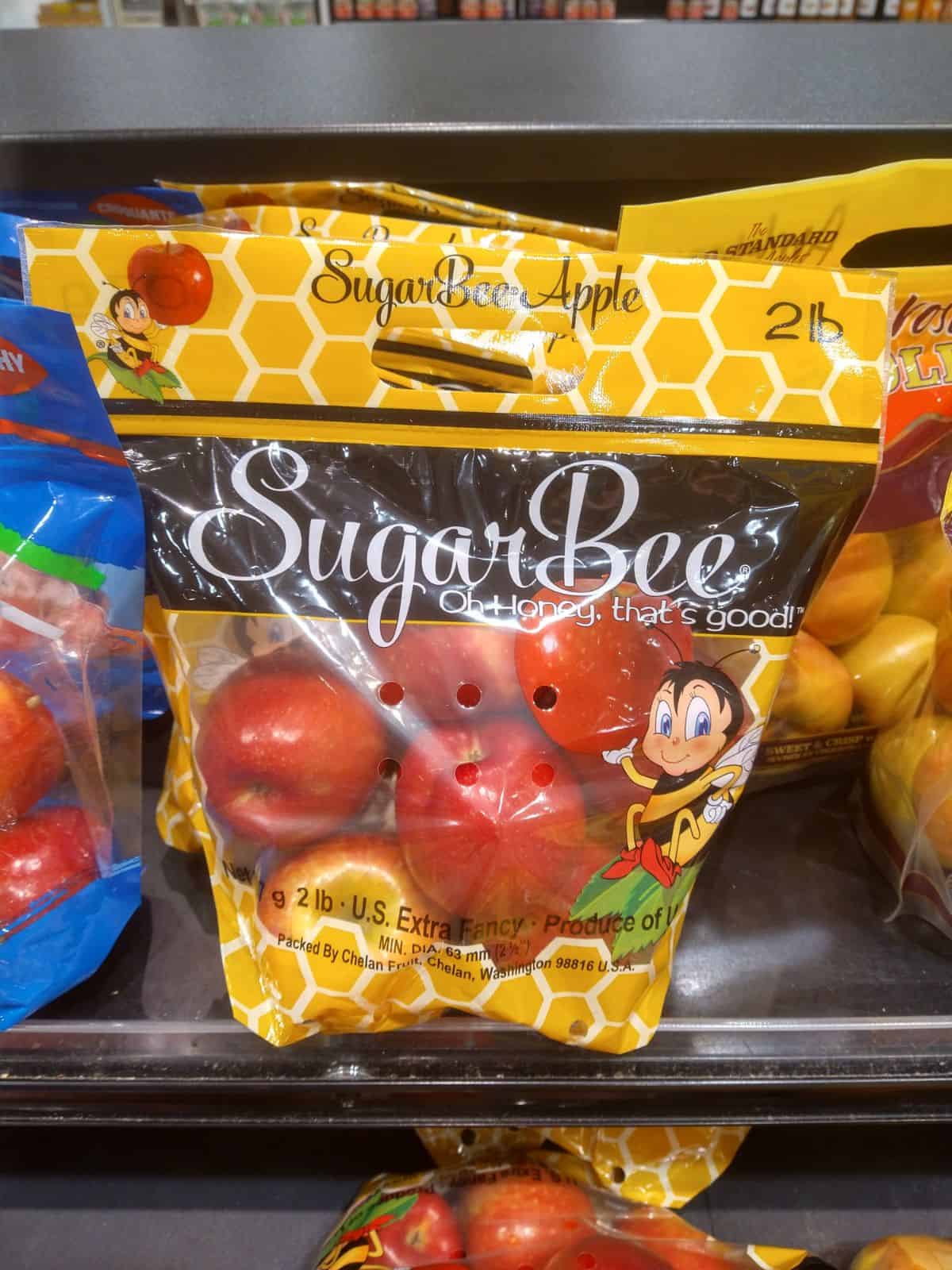 A bags of Sugar Bee Apples pictured in the grocery store. The bag has honeycombs on it and a cartoon bee holding an apple.